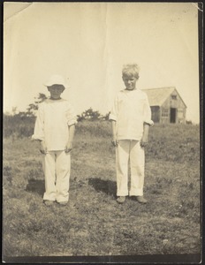 Two boys dressed in white standing on hill with barn in background