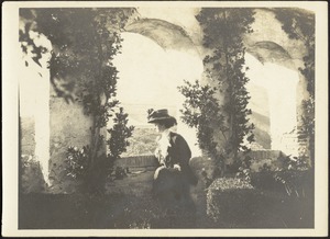 Helen Stevens (Coolidge) wearing wide hat looking out at landscape below from arched window on brick/stone garden terrace