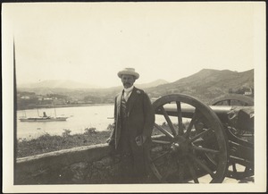 John Gardner Coolidge standing next to cannon on terrace overlooking harbor