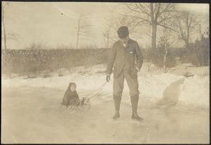 Man in fur hat and skates pulling small child on sled across frozen lake near shore
