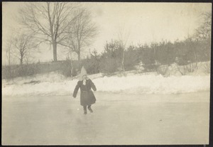 Small girl in pointed hat skating on frozen lake near shore