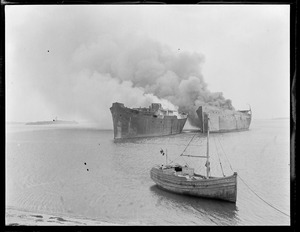 Shipping board boats burn for scrap. Small fishing boat in front.