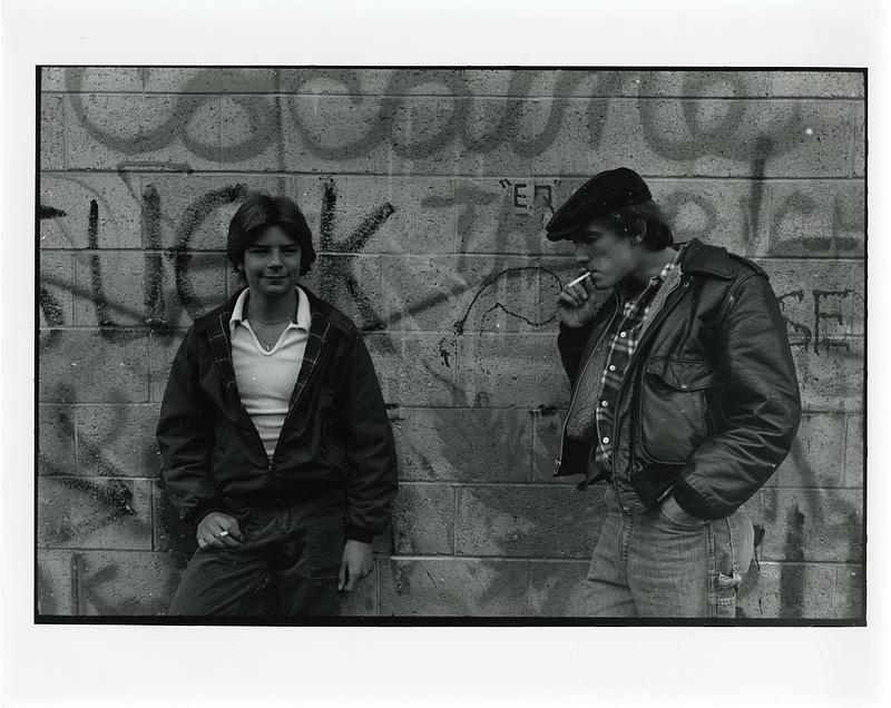 Two teenagers smoking against wall