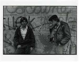 Two teenagers smoking against wall