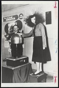 Atomic Hair Do -- John Jameson of the Associated Universities, Inc., holds an electrode, the miniature Van De Graaff electrostatic generator setting off a charge up to 125,000 volts (200 micro amps), which causes Jean Klein’s hair to stand on end at an exhibit in New York.