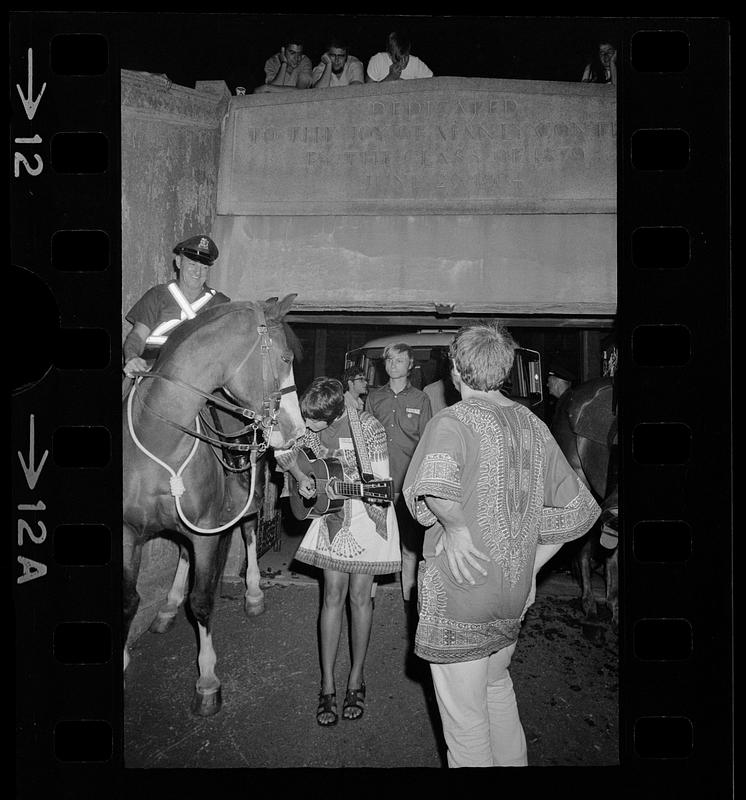 A pregnant Joan Baez serenades a cop's horse at Harvard Stadium, Brighton