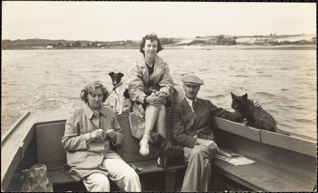 A man and two women sit in a boat with three small dogs