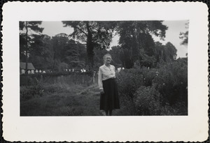 An older woman stands among tall field grasses