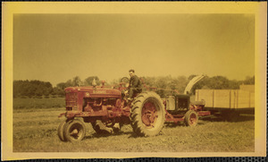A man sits astride a large, red Farmall tractor