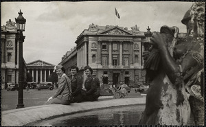 Three women, dressed in military-style uniforms, sit on the edge of a fountain