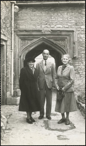 Two women and a man stand in front of a carved stone arch