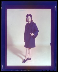 A woman stands in uniform in a coat with a purse.
