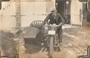 Albert T. Chase on motorcycle in front of garage at the Cape Cod Laundry, West Yarmouth, Mass.