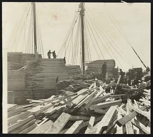 Lumber for Boston. At left, the bow of the schooner Alvena and, at right, loading 750,000 feet of New Brunswick spruce on the four-masted ship, one of the few of her kind remaining in Atlantic waters