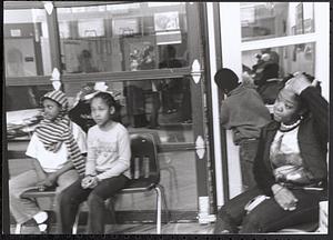 Young girls and a woman sitting in chairs and watching an activity