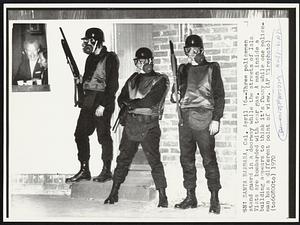 Three policemen stand guard in a doorway while the streets of Isla Vista are bombarded with tear gas. A man inside a building appears to think it's funny while one policeman has a different point of view.