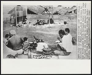 Quake Victims Camp Out-These residents of Fukui, Japan made homeless by the earthquake which ravaged their city June 28, squat in the open to eat meager fare salvaged from wrecked homes shown in background.