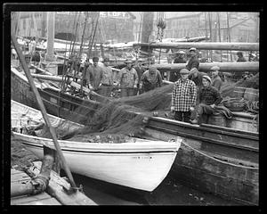 Fishermen pose with their nets on a fishing boat next to a smaller boat "Good Luck"