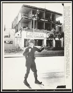 National Guardsman Chuck Larson aids in traffic control, while on guard to prevent looting of 'quake-devastated stores and residences. Walls were ripped off the Mission Hotel (backgd), but fortunately, no one was injured in the hotel.