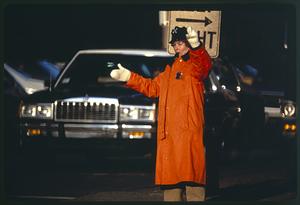 Woman police officer directs traffic in orange raincoat, Boston