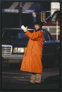 Woman police officer directs traffic in orange raincoat, Boston