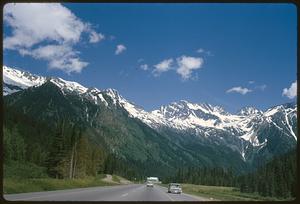 View down road at foot of mountains covered in trees and snow, British Columbia
