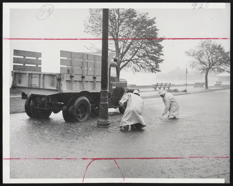 Roads Flooded-Metropolitan District Commission employes stand knee deep in water on Strandway as they work to open sewers plugged during heavy rains drivn by winds of gale force from hurricane.