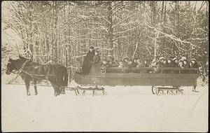 Large horse-drawn sleigh in winter, with many people on board