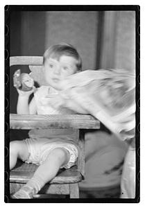 A toddler in a high chair holding an alarm clock