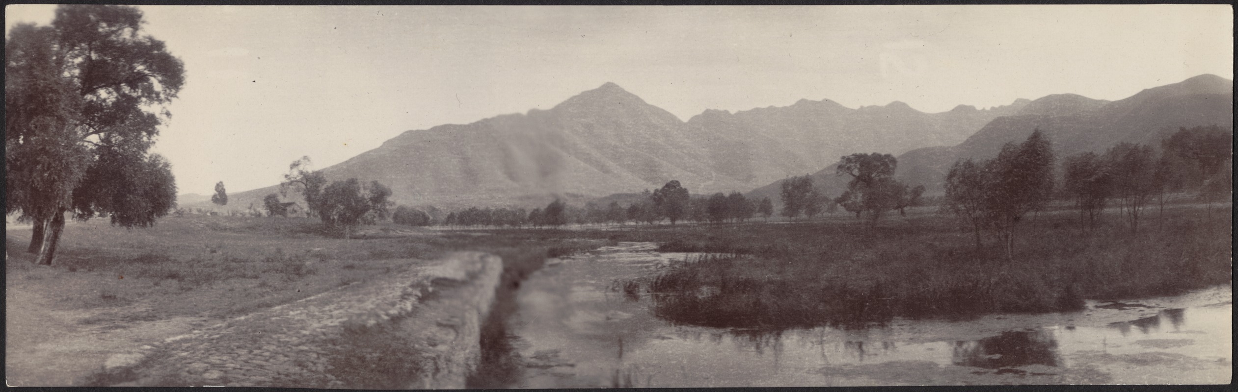 Road by a river and field; mountains in distance