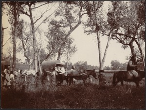 Chinese villagers and one western man in wide-brimmed hat traveling in horse-drawn covered wagons