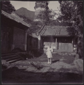 Chinese man in white standing in courtyard; temple tower in distance