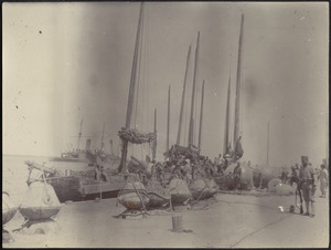 Unidentified harbor with sailing vessel in dock; unidentified battleship on left in distance; soldier with gun in foreground