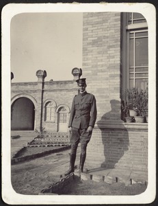 Unidentified man in military uniform standing in front of brick building