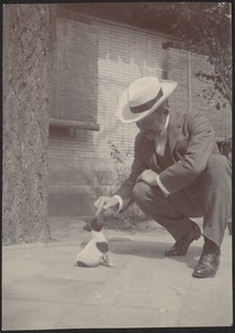 John Gardner Coolidge's house in Peking — Unidentified man in white wide-brimmed hat kneeling next to small puppy in main courtyard