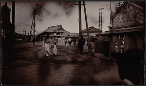 Street scene in Japan; people in kimonos walking down street near shops