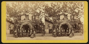 Group photograph of twelve people at the entrance to Vine Cottage, with two additional people on the balcony