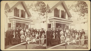 Group portrait of thirty-six people seated and standing in front of cottages