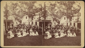 Group portrait of people, with cottages partially visible in the background