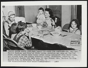 Soup for Refugees--Mr. and Mrs. Walter Barkley and five of their seven children eat soup at the Red Cross relief center here today after being evacuated from their home, six blocks from the rising Missouri river. Clockwise, starting in foreground: Carol, 10; Mary Ann, 6; the father; Mrs. Barkley holding Sandra Sue, 1; Kathleen, 9, and Eva, 7.