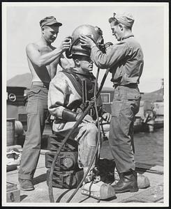 Preparations Sgt. Dawson Merchant, of an army engineer construction company, is assisted into his deep sea diving helmet preparatory to submerging in the waters off Korea, during a salvage operation. Other engineer personnel include Cpl. Donald A. Ackerberg and Cpl. Clayton J. Shufelt.