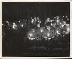 Seabees somewhere in the western Pacific bow their heads in prayer during a candle-light holy communion service