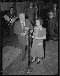 Unidentified man and woman at WNAC microphone with band behind them