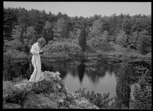 Woman with camera standing at water's edge looking down