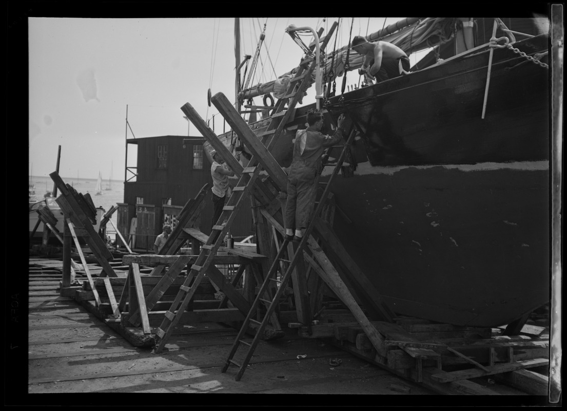 Men on ladders working on a sailboat in dry dock