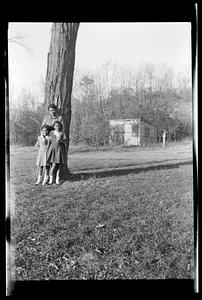 Yvonne and two girls stand under a tree, shed in background
