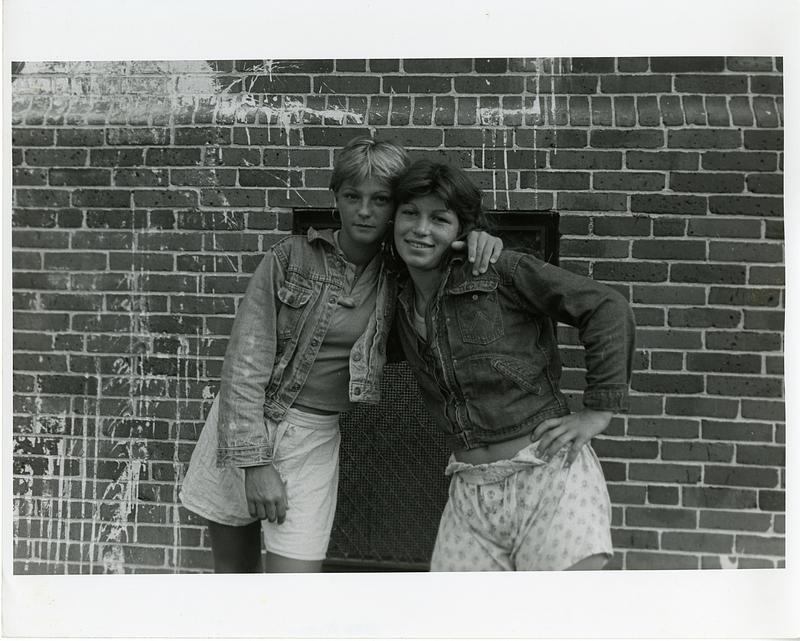 Portrait of two teenage girls embracing in front of a brick wall