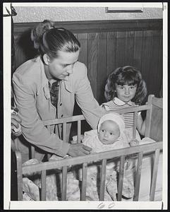 A Tiny Storm Refugee is sheltered in Revere at the Red Cross center at Our Lady of Lourdes Church. The baby is three-months-old Paul Hurley shown with his mother, Mrs. Leo Hurley, and his sister, Lee, 4.