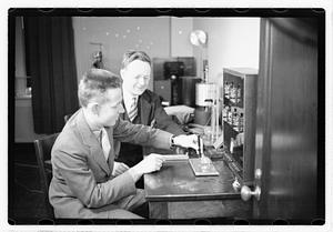 A boy sitting next to a man using an unidentified device