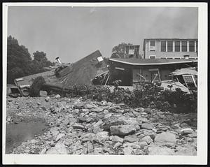 The Roof Fell In-In Charlton, the wreckage of part of the Charlton Woolen Mills, isolated by flood waters, lurches crazily along shore line. Charlton was one of the Massachusetts communities most severely hurt by the flood, which left thousands of workers jobless in industrial sections of the state, Connecticut and Rhode Island. Raging waters hurled huge boulders around, causing great destruction.
